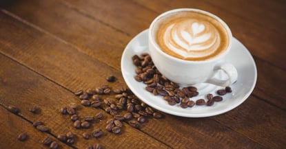 Cup of cappuccino with coffee art and coffee beans on wooden table_adobespark